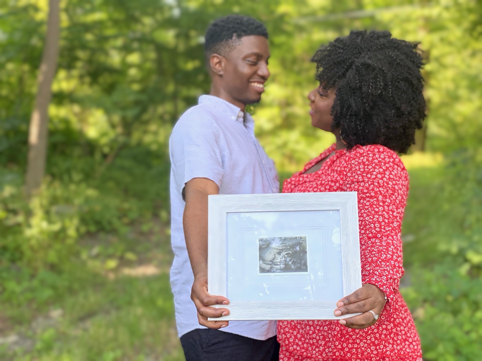 An expecting couple sharing a tender moment outdoors, holding a framed sonogram.