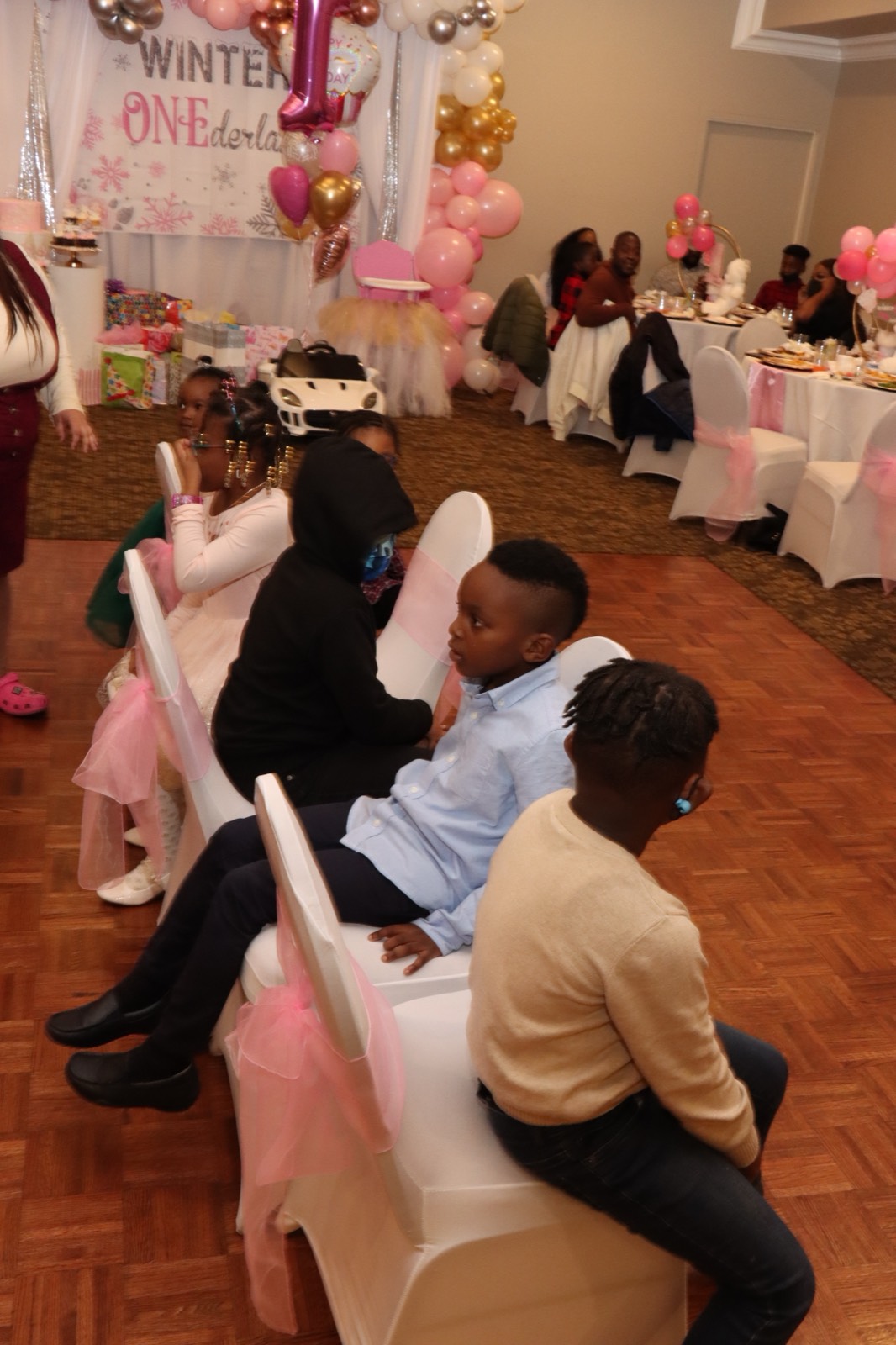 Young guests seated together watching the festivities at the pink first-birthday celebration.